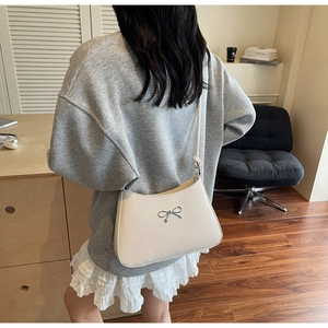 Close-up of cream shoulder bag with silver bow hardware and thin strap detail