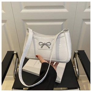 Détail du sac à bandoulière blanc motif crocodile avec nœud argenté sur une chaise