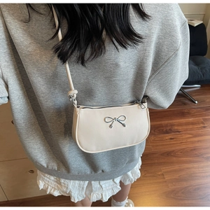 Close-up of minimalist off-white crescent bag with silver metal bow and smooth finish