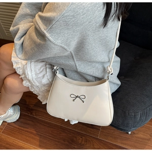 Detailed view of a cream shoulder bag featuring a silver metal bow accent and sleek design