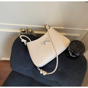 Detail of cream-white shoulder bag with silver bow accent on a dark blue corduroy sofa