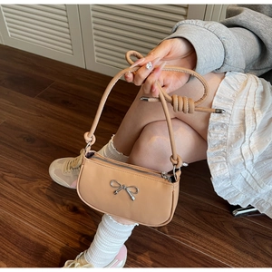 Detail of apricot crescent bag featuring a silver bow buckle and knotted shoulder strap