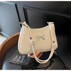 Close-up of beige underarm bag with silver bow detail and knotted shoulder strap
