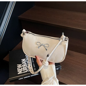 Close-up of cream crescent underarm bag with silver bow detail and knotted shoulder strap