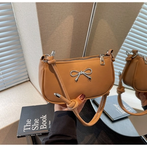 Detail of silver bow accent and knotted strap on a khaki crescent shoulder bag
