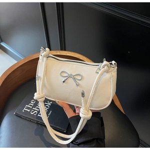 Detail of a creamy white underarm bag with a silver metal bow and knotted strap design