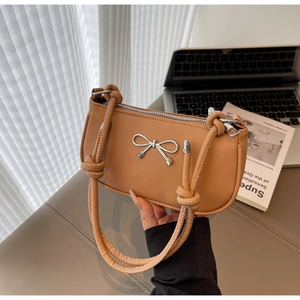 Detail of light brown underarm bag with silver bow ornament and elegant knot shoulder strap
