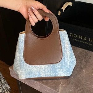 Blue denim bucket bag with brown leather trim and rhinestone accents held by hand