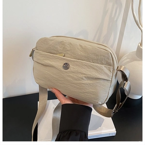 Detail of beige nylon crossbody bag with adjustable fabric strap and round metal logo