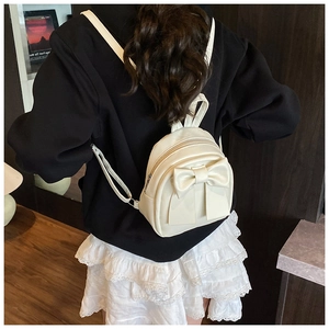 Detail of white PU leather mini backpack featuring a large bow and double zipper closure