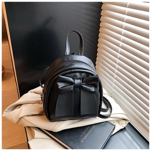 Detail of black mini backpack featuring a large bow on cream blazer background