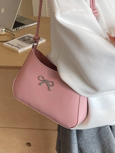 Pink faux leather hobo bag with silver bow detail, worn by model in cozy indoor setting