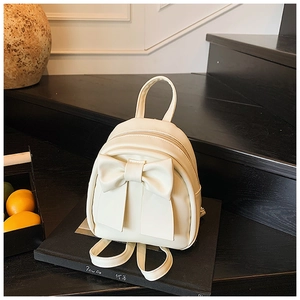 Close-up of cream bow backpack with 3D ribbon detail on a decorative display stand
