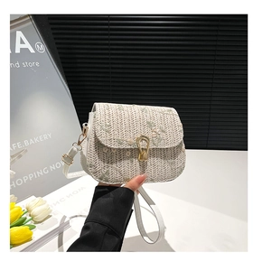 Close-up of white woven straw saddle bag featuring floral embroidery and gold clasp