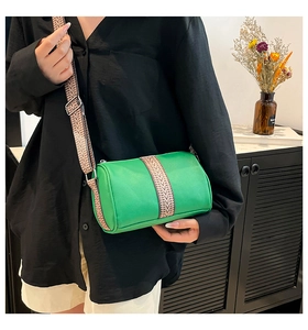 Cylindrical green leather bag with a wide ethnic style woven strap and silver hardware