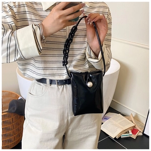 Detail of a shiny black mini crossbody bag featuring a large pearl clasp and chain strap