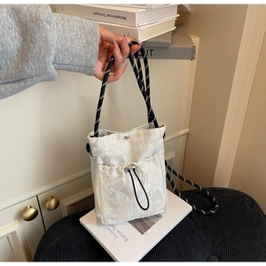Detail view of floral butterfly embroidery and woven cotton strap on a white bucket bag