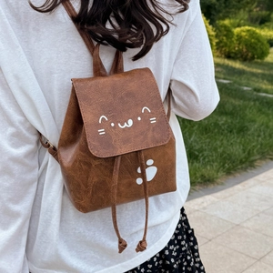 Brown faux leather mini backpack with cute cat print and bow detail shown on a model outdoors