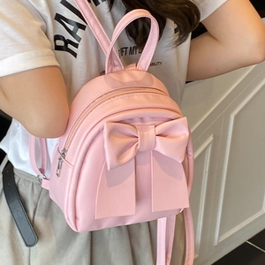 Pink mini faux leather backpack with large bow detail shown on model in a summer style