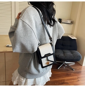 Detail shot of a black and white woven leather crossbody bag with gold charm on a model