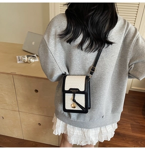 Detail of crossbody phone bag with white croc texture and elegant gold pendant on black flap