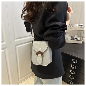 Détail d'un sac bandoulière gris avec boucle en bois et fermoir en métal sur le rabat