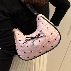 Sac lune plissé rose avec imprimés nœuds noirs et pendentif cœur porté sur l'épaule