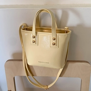 Sac seau vintage crème avec poignées et bandoulière sur une chaise en bois