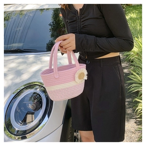 Detail of pink and beige woven handbag with daisy floral accents held by a person outdoors