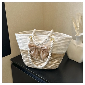 Detail of hand-woven beige and brown tote bag featuring a large satin bow decoration