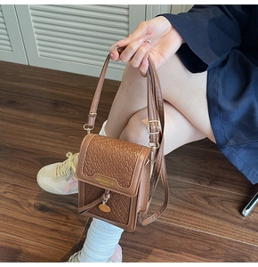 Detail of brown faux leather mini crossbody bag with crocodile texture and woven pattern