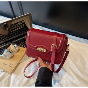 Macro detail of wine red leather flap and golden cylindrical twist lock on the crossbody bag