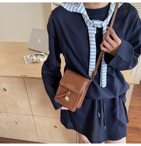 Close-up of brown woven leather phone bag with gold metal pendant and thin strap