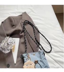 Hellblaue Mini-Umhängetasche aus Nylon mit Kordelgurt und Plüschanhänger auf weißem Laken
