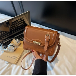 Detail of a brown PU leather crossbody bag with a gold buckle on a white bed sheet