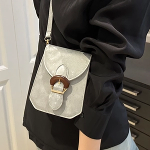 Petit sac bandoulière gris clair en daim avec boucle en bois porté sur une chemise noire