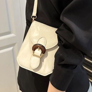 Sac à bandoulière beige chic avec boucle ronde en bois et détails dorés sur un mannequin