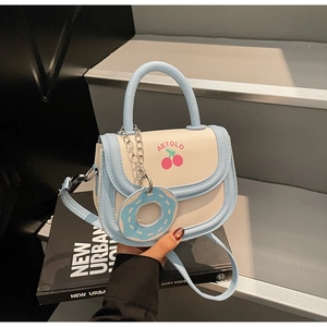 Close-up of cream and light blue saddle bag featuring cherry print and donut charm detail