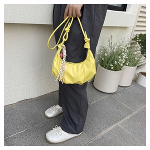 Detail of bright yellow crescent bag featuring knotted handle and woven tassel charm