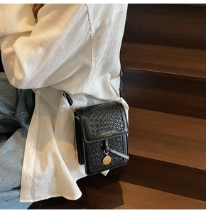 Close-up of black textured faux leather mini crossbody bag with gold rectangular plaque