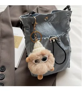 Kleiner Plüsch-Taschenanhänger mit großen Augen und weißer Mütze an blauer Tasche