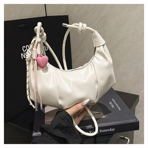 Close-up of white pleated hobo bag with knotted handle and pink heart pendant accessory