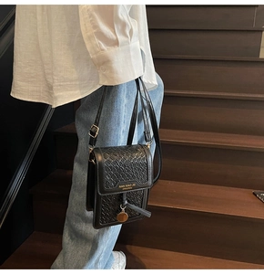 Detailed close-up of a black woven leather phone bag featuring a gold pendant on stairs