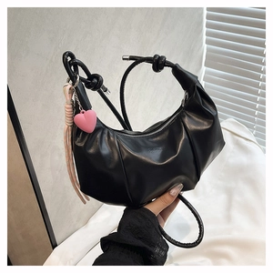 Detail of black pleated saddle bag featuring a pink heart pendant and fashion logo
