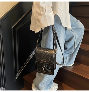 Detail of black woven texture crossbody bag with metal charm on casual outfit