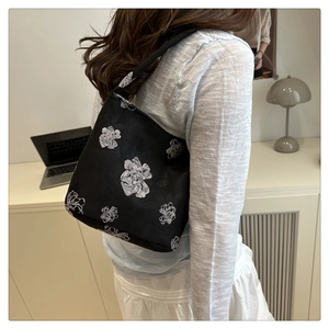 Lifestyle shot of a Chinese style embroidered bucket bag with white floral patterns on black
