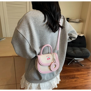 Detail view of mini cream and pink saddle bag with cherry pattern and pink shoulder strap