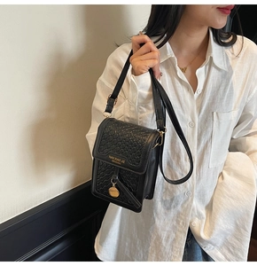 Detail of black woven leather crossbody phone bag with gold logo and metallic charm