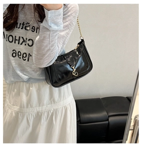 Détail du sac en cuir verni noir brillant avec fermoir à piston doré et bandoulière