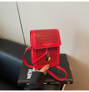 Detailed view of red woven leather phone crossbody bag with gold lettering and charm
